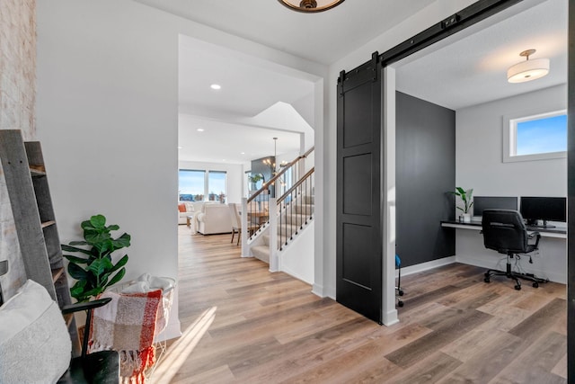 home office with a barn door, light hardwood / wood-style flooring, and an inviting chandelier