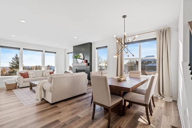 dining area with hardwood / wood-style floors, a notable chandelier, a large fireplace, and a healthy amount of sunlight