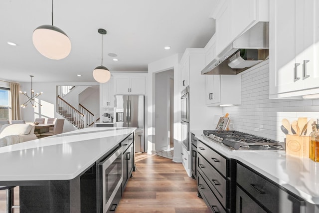 kitchen featuring white cabinets, decorative light fixtures, wall chimney range hood, and stainless steel appliances