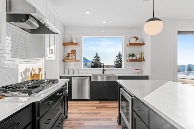 kitchen featuring sink, stainless steel appliances, pendant lighting, white cabinets, and exhaust hood