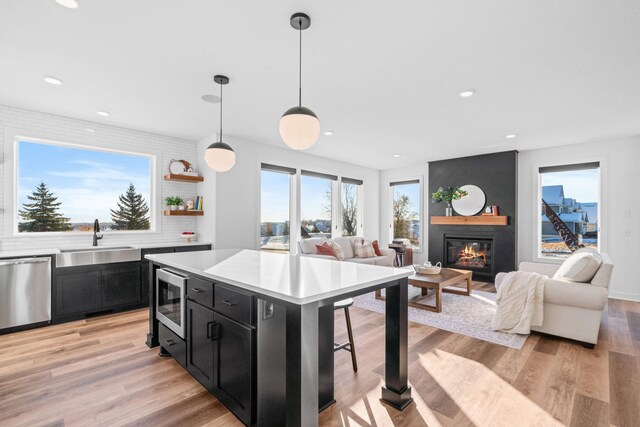 kitchen with a center island, sink, hanging light fixtures, stainless steel appliances, and light hardwood / wood-style flooring