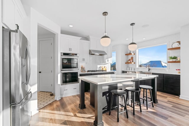 kitchen with pendant lighting, ventilation hood, white cabinets, tasteful backsplash, and stainless steel appliances