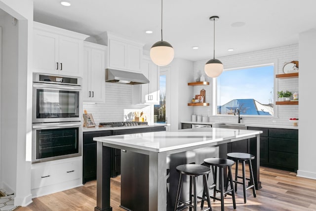 kitchen featuring decorative backsplash, stainless steel appliances, exhaust hood, white cabinets, and a kitchen island