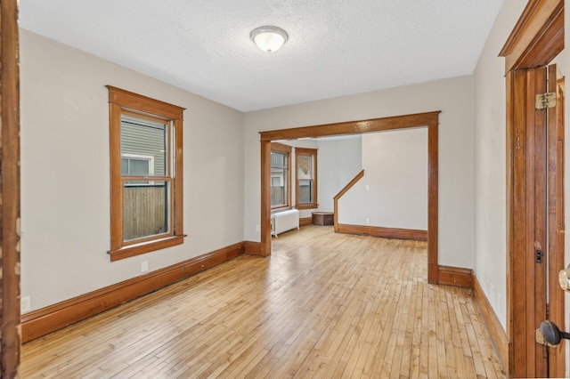 empty room with a textured ceiling, light wood-type flooring, radiator heating unit, and a wealth of natural light