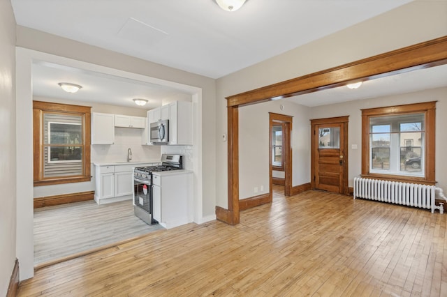 kitchen with radiator heating unit, light hardwood / wood-style floors, plenty of natural light, and appliances with stainless steel finishes