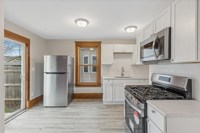 kitchen featuring sink, tasteful backsplash, light hardwood / wood-style floors, white cabinets, and appliances with stainless steel finishes