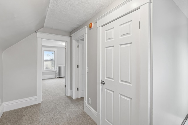 corridor with light carpet, a textured ceiling, vaulted ceiling, and radiator