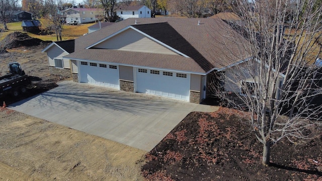 view of front of property with a shingled roof, stone siding, an attached garage, and concrete driveway