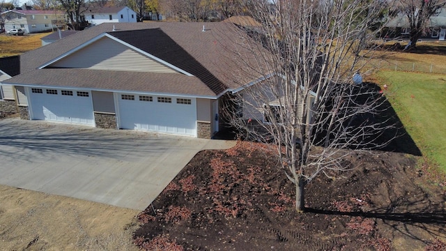 single story home featuring concrete driveway, stone siding, roof with shingles, and an attached garage