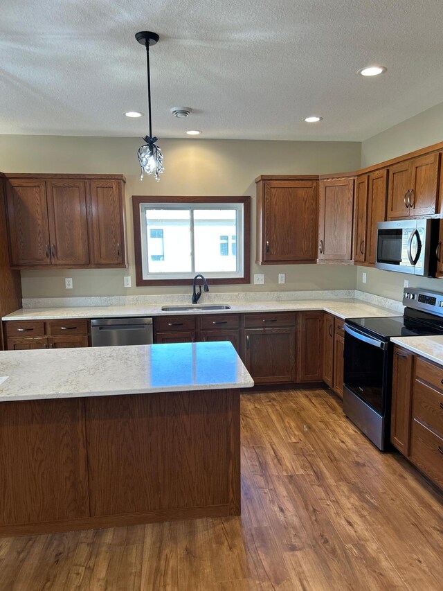 kitchen featuring a textured ceiling, stainless steel appliances, wood finished floors, a sink, and pendant lighting