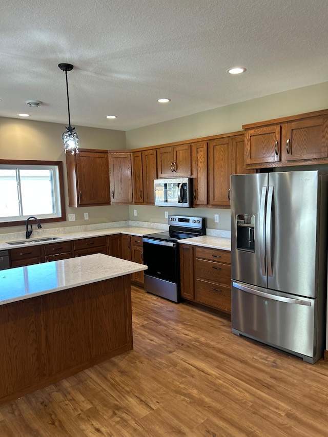 kitchen with brown cabinets, wood finished floors, stainless steel appliances, light countertops, and pendant lighting