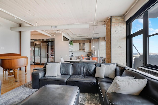 living room with brick wall, rail lighting, and wood-type flooring