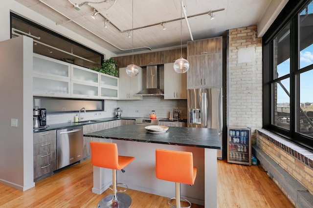 kitchen featuring wine cooler, wall chimney exhaust hood, a kitchen breakfast bar, a kitchen island, and stainless steel appliances