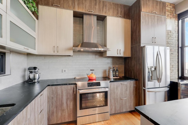 kitchen featuring appliances with stainless steel finishes, wall chimney exhaust hood, light wood-type flooring, and backsplash