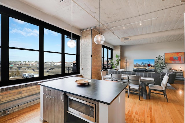 kitchen with pendant lighting, a center island, stainless steel microwave, brick wall, and light wood-type flooring