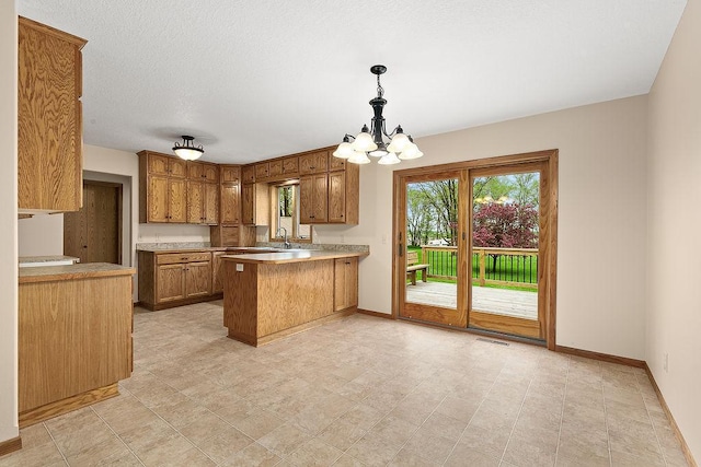 kitchen featuring sink, an inviting chandelier, kitchen peninsula, pendant lighting, and a textured ceiling