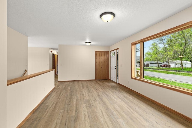 empty room featuring light wood-type flooring, a textured ceiling, and baseboards