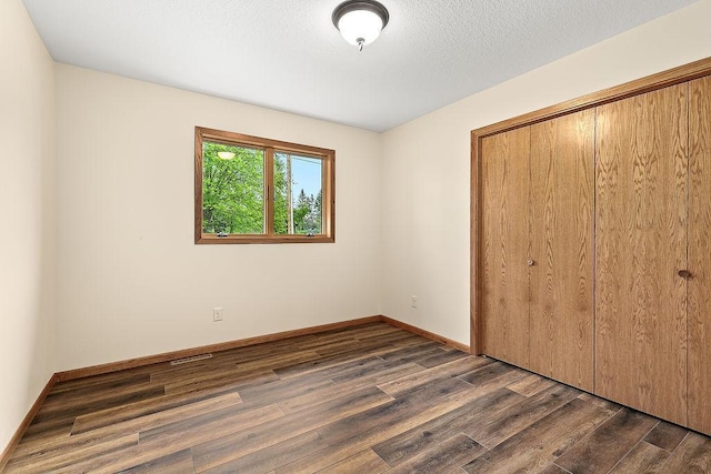 unfurnished bedroom with dark wood-style floors, a closet, a textured ceiling, and baseboards