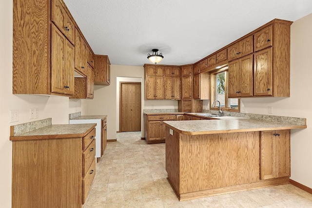 kitchen featuring brown cabinets, light countertops, a sink, a peninsula, and baseboards