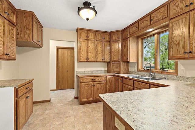 kitchen featuring light countertops, brown cabinetry, a sink, a textured ceiling, and baseboards