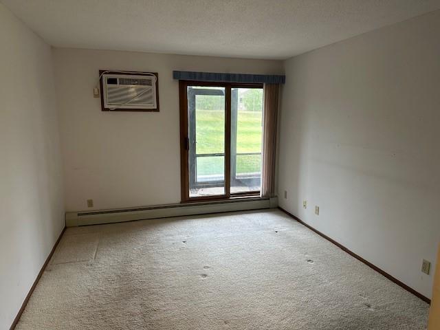 empty room featuring a textured ceiling, baseboard heating, a wall unit AC, and light carpet