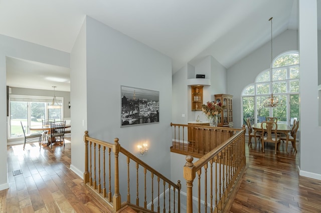 hall featuring a chandelier, high vaulted ceiling, an upstairs landing, and wood finished floors