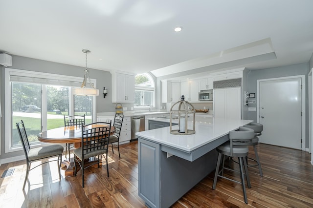 kitchen featuring decorative light fixtures, light countertops, white cabinetry, a kitchen island, and built in appliances