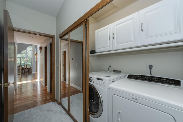 clothes washing area featuring light colored carpet, baseboards, washer and dryer, light wood-type flooring, and cabinet space