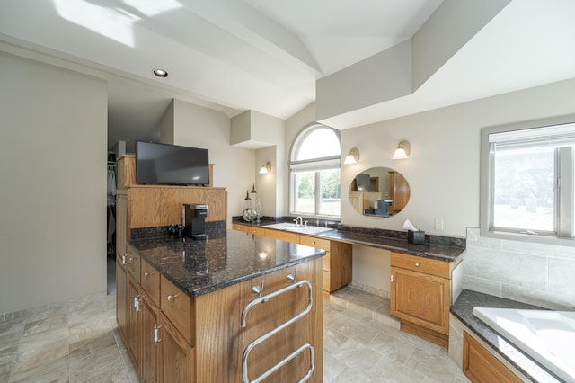 kitchen with a sink, vaulted ceiling, a center island, brown cabinetry, and dark stone countertops