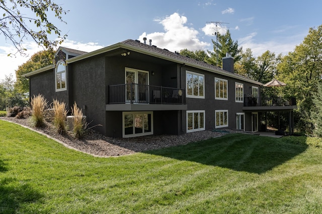 back of house with stucco siding, a chimney, and a yard