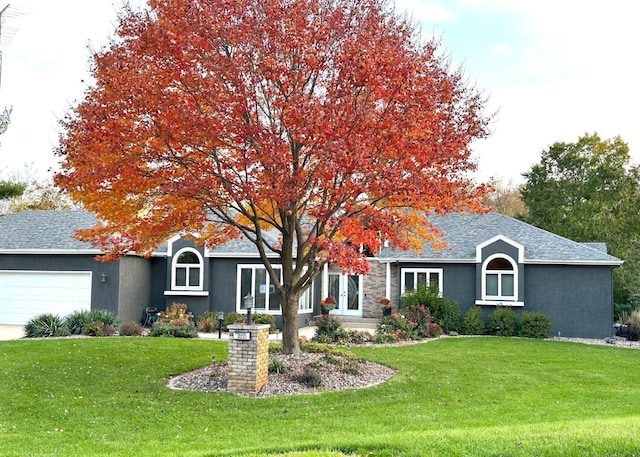 view of property hidden behind natural elements with a garage, roof with shingles, a front yard, and stucco siding