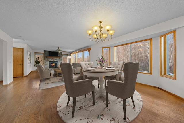 dining area featuring a textured ceiling, ceiling fan with notable chandelier, light hardwood / wood-style flooring, and a stone fireplace