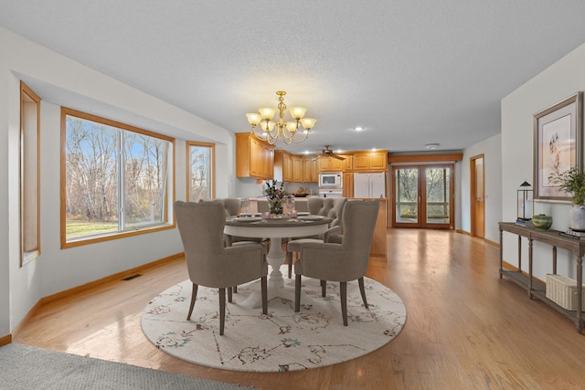 dining room featuring ceiling fan with notable chandelier, a textured ceiling, and light wood-type flooring