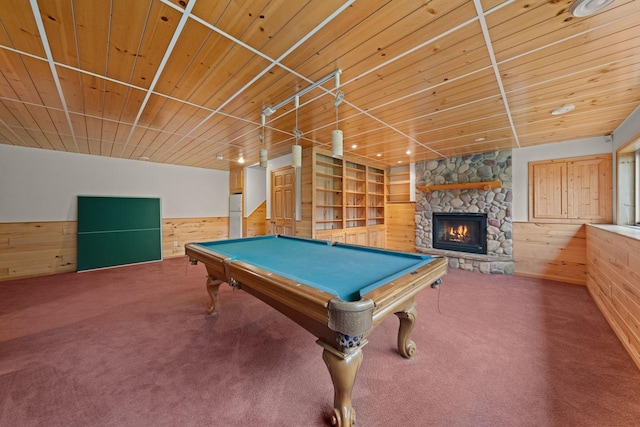 rec room featuring wood walls, a stone fireplace, carpet floors, and wooden ceiling