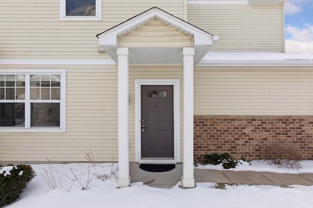 snow covered property entrance featuring brick siding