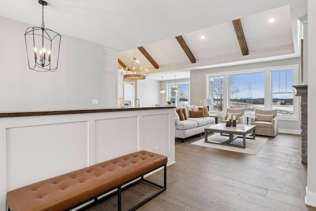 living room with a chandelier, sink, light hardwood / wood-style flooring, and lofted ceiling with beams