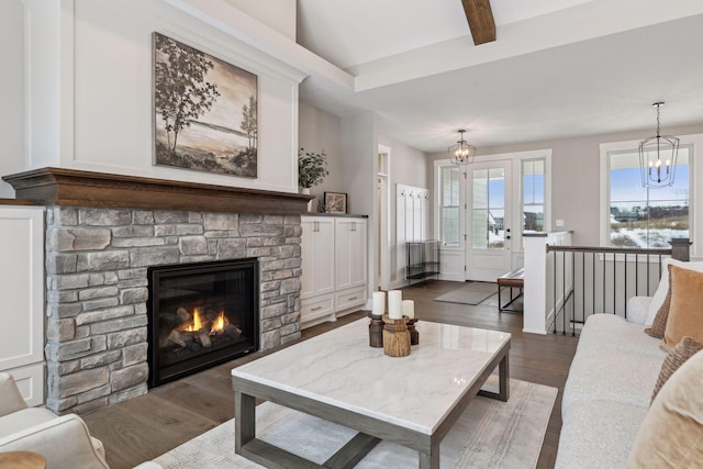 living room featuring dark wood-type flooring, beamed ceiling, a notable chandelier, and a fireplace