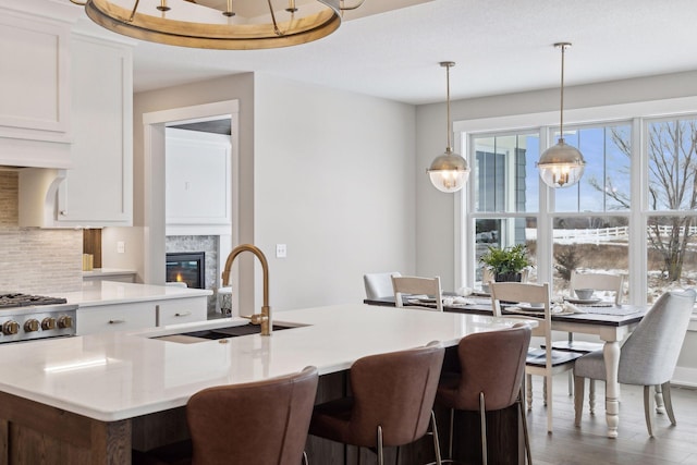 kitchen with white cabinetry, tasteful backsplash, decorative light fixtures, a fireplace, and sink