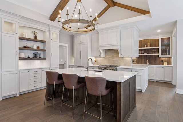 kitchen with a breakfast bar area, backsplash, a kitchen island with sink, white cabinets, and sink