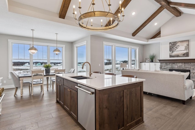 kitchen with a stone fireplace, an island with sink, dishwasher, hanging light fixtures, and sink