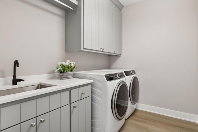 washroom featuring washer and dryer, light hardwood / wood-style flooring, sink, and cabinets