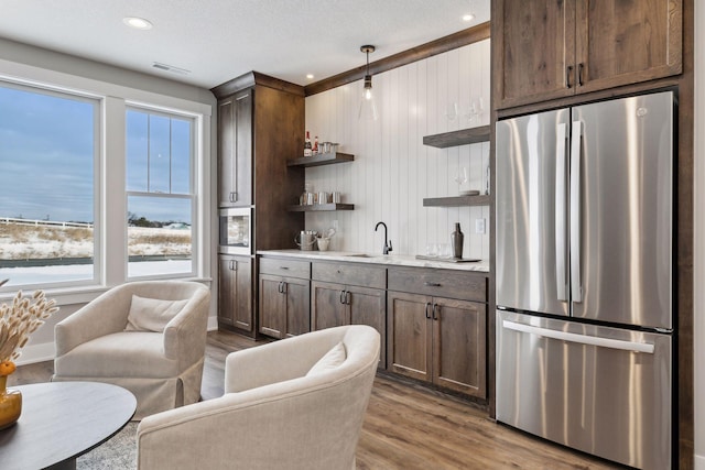 kitchen featuring sink, hardwood / wood-style floors, dark brown cabinetry, and stainless steel refrigerator