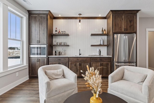 kitchen featuring appliances with stainless steel finishes, dark wood-type flooring, pendant lighting, dark brown cabinetry, and sink