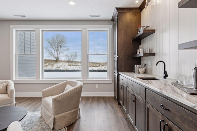 bar featuring light stone countertops, a wealth of natural light, dark brown cabinetry, and sink