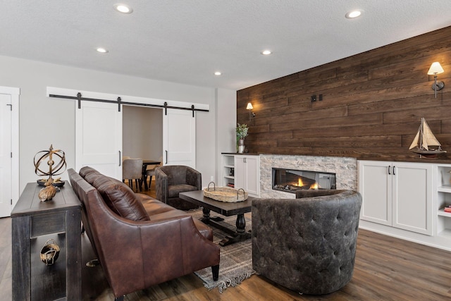 living room with a textured ceiling, dark hardwood / wood-style floors, a stone fireplace, and a barn door