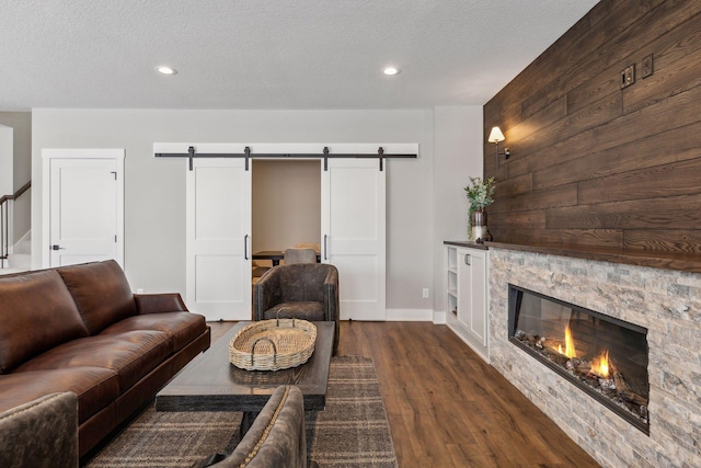 living room featuring a barn door, wooden walls, a stone fireplace, a textured ceiling, and dark hardwood / wood-style flooring