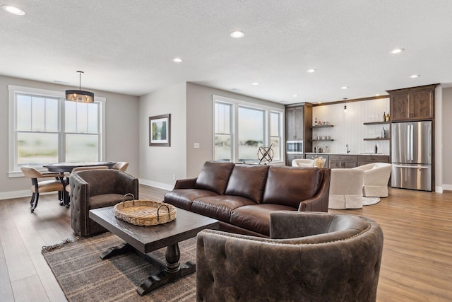 living room with sink, a textured ceiling, light hardwood / wood-style flooring, and a healthy amount of sunlight