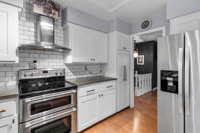 kitchen with wall chimney exhaust hood, stainless steel appliances, backsplash, light hardwood / wood-style floors, and white cabinets