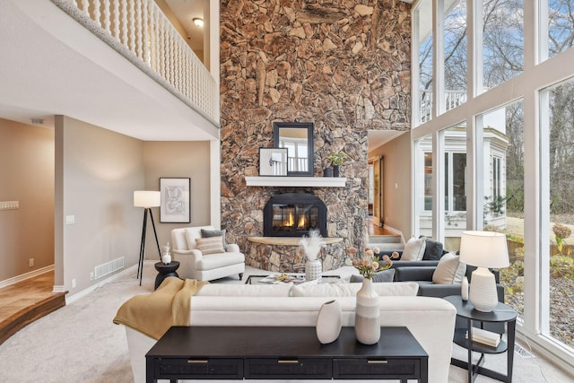 living room with a stone fireplace, light carpet, and a high ceiling