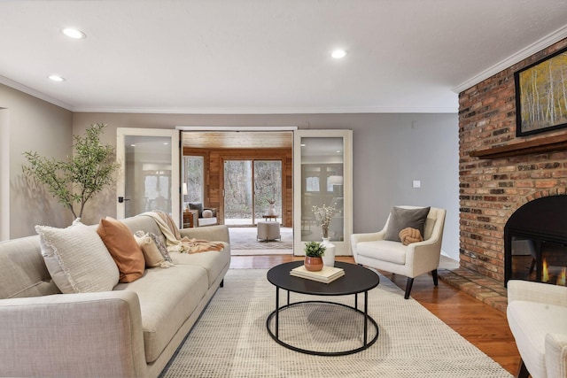 living room with crown molding, wood-type flooring, and a brick fireplace